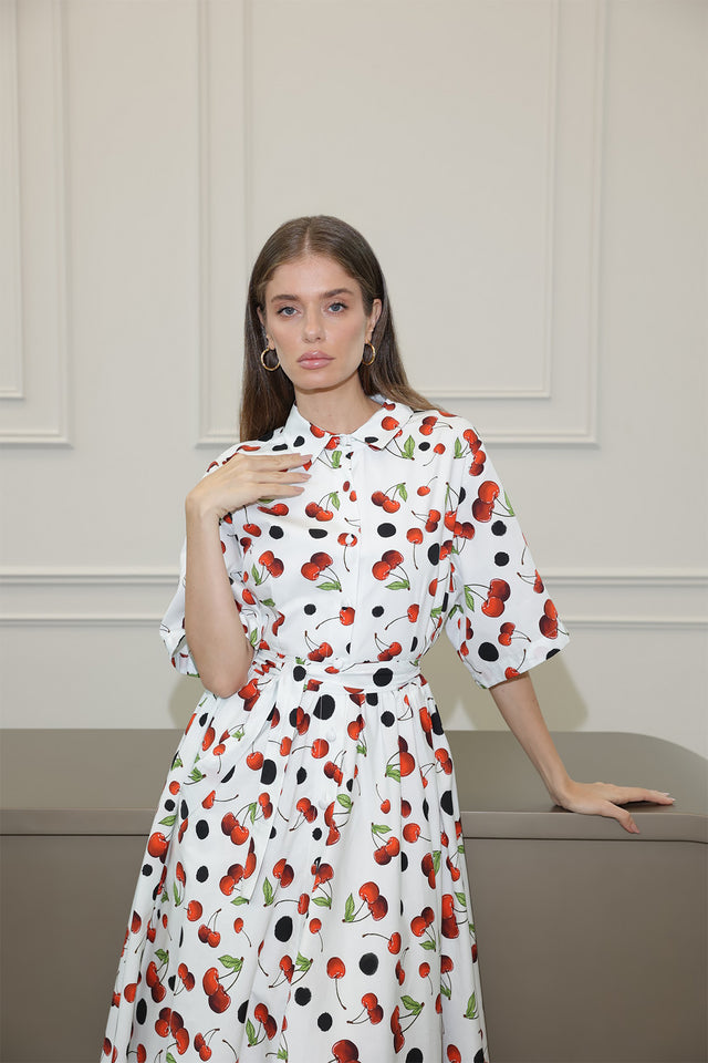 Woman wearing a white dress with red and black cherry pattern against a neutral background