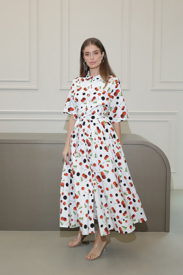 Woman wearing a white dress with red and black floral pattern against a neutral background